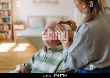 Operatore sanitario pettinando i capelli dell'uomo anziano in camera da letto a casa Foto Stock