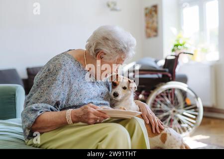 Donna anziana felice che tiene un piatto di cibo e accarezza il cane a casa Foto Stock