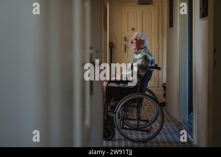 Uomo anziano contemplativo seduto in sedia a rotelle a casa Foto Stock