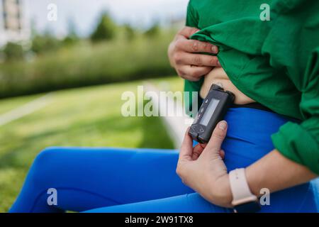 Donna con diabete si esercita all'aperto in città, controllando il suo livello di zucchero nel sangue su una pompa di insulina. Foto Stock