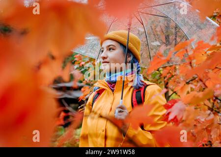 Donna sorridente che tiene un ombrello nel parco autunnale Foto Stock