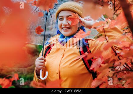 Donna sorridente che tiene la foglia sul viso nel parco autunnale Foto Stock