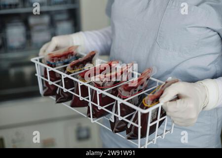 Mani di operatore sanitario tenendo rack di sacche di sangue Foto Stock
