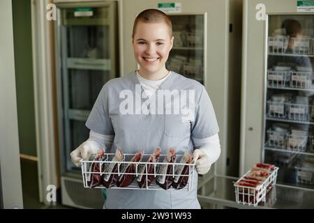 Un tecnico di laboratorio sorridente che tiene in clinica un rack di sacche di sangue Foto Stock