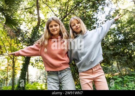 Ragazze sorridenti con le braccia alzate in piedi davanti agli alberi al parco Foto Stock