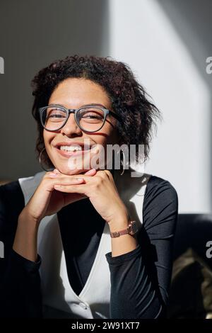 Giovane donna d'affari sorridente che indossa occhiali da vista seduta in ufficio Foto Stock
