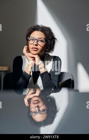 Giovane donna d'affari che indossa occhiali da vista seduta alla scrivania in ufficio Foto Stock