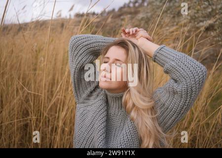 Donna bionda che indossa un maglione grigio vicino all'erba alta asciutta Foto Stock