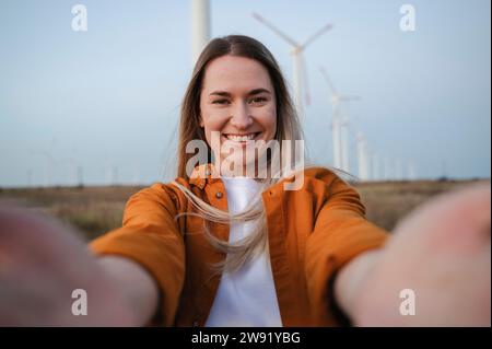 Donna sorridente che scatta selfie davanti alle turbine eoliche Foto Stock