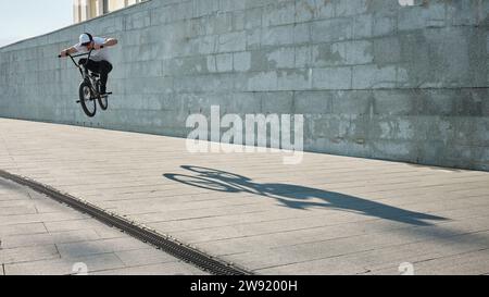 Uomo che fa acrobazie con la bici BMX davanti al muro Foto Stock