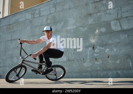 Uomo che indossa il berretto e fa acrobazie con la bici BMX davanti alla parete Foto Stock