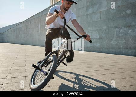 Uomo che fa acrobazie con la bici BMX davanti alla parete nelle giornate di sole Foto Stock