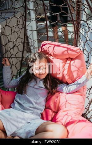 Ragazza sorridente che riposa sull'altalena del portico Foto Stock