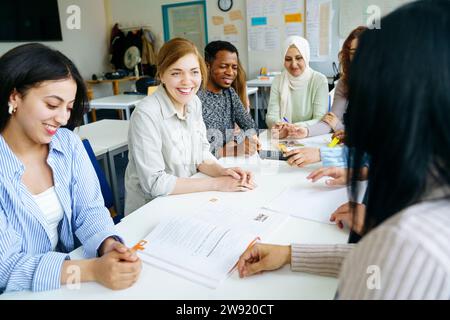Sorridenti studenti multietnici che studiano insieme alla scrivania in classe Foto Stock