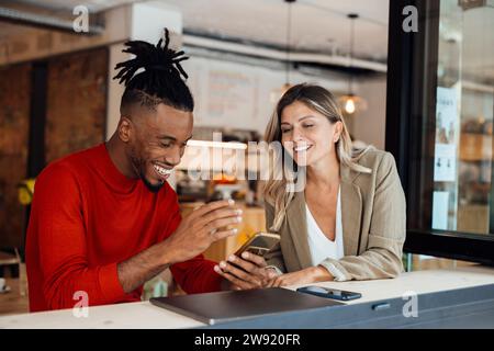 Collega felice che usa lo smartphone da una donna d'affari al bar Foto Stock