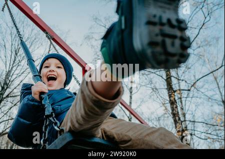 Un ragazzo allegro che gioca a swing al parco sotto il cielo Foto Stock