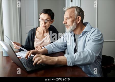 Coppia anziana che parla di problemi di famiglia mentre si siede al tavolo davanti al notebook a casa Foto Stock