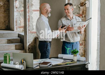 Architetti sorridenti che discutono insieme su campioni di piastrelle alla scrivania in ufficio Foto Stock