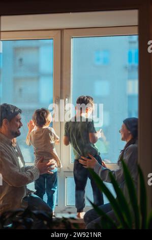 Genitori che tengono bambini che guardano fuori dalla finestra a casa Foto Stock