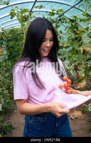 Donna sorridente che cattura pomodori con una t-shirt rosa Foto Stock