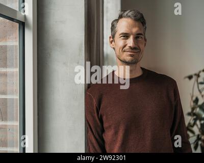 Uomo appoggiato al muro vicino alla finestra di casa Foto Stock