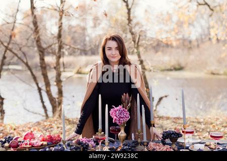 Donna in piedi vicino a un tavolo decorato preparata per la celebrazione del Ringraziamento nella foresta Foto Stock