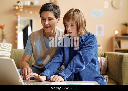 Madre che insegna a una figlia con sindrome di Down ad usare il portatile a casa Foto Stock