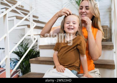 Madre sorridente con la mano nei capelli di un figlio seduto sulle scale a casa Foto Stock