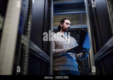 Giovane ingegnere IT che lavora su un notebook nella sala server dati Foto Stock