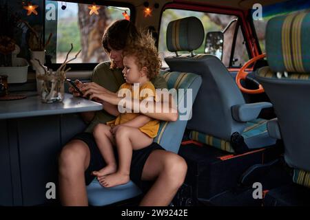 Fratello che usa uno smartphone seduto con sorella in caravan Foto Stock