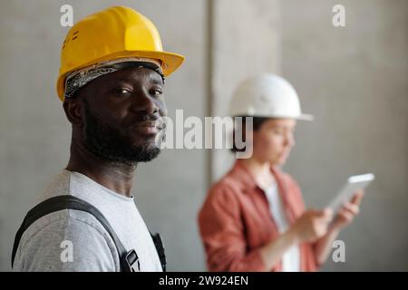 Operaio edile che indossa elmetto con ingegnere sullo sfondo Foto Stock