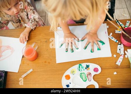 Ragazza che fa l'impronta della mano con gli acquerelli sulla carta a casa Foto Stock