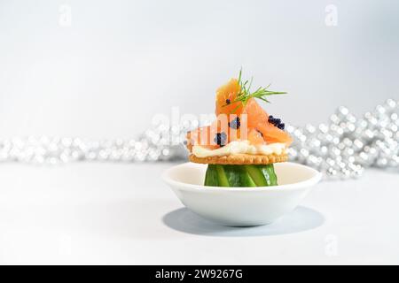 Spuntino o antipasto con salmone affumicato, cetriolo intagliato, cracker e caviale con contorno di aneto, servito a forma di fungo su un piccolo piatto bianco, f Foto Stock