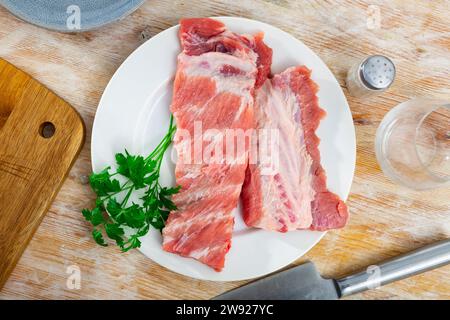 Rastrelli di costolette di maiale crude fresche sul piatto con prezzemolo e coltello Foto Stock