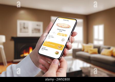 Smartphone con un'app fast food in mano, donna che si sta godendo pizza e hamburger in un accogliente sottofondo del soggiorno. Ordina ora per una deliziosa festa Foto Stock