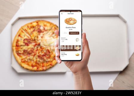 Donna ordina e apprezza una pizza Quatro, consegnata alla sua scrivania tramite una moderna app per smartphone. Design senza cuciture per una deliziosa esperienza culinaria Foto Stock