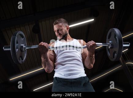 Immagine di un ragazzo muscoloso in una maglia bianca con attrezzature sportive. Palestra. Concetto di fitness Foto Stock