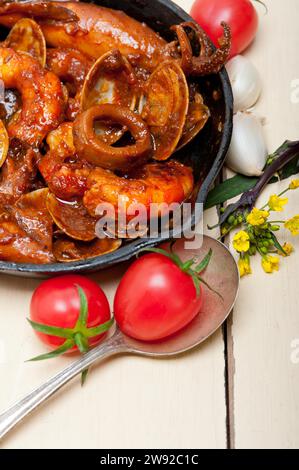 Stufato di pesce fresco preparato su una padella di ferro da stiro su un tavolo di legno rustico bianco, fotografia gastronomica Foto Stock