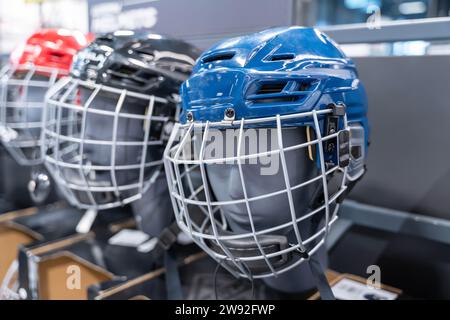 Una collezione di caschi da hockey dalle nuance blu e rosse, ciascuno dotato di visiera, ordinatamente presentato su uno scaffale di un negozio di attrezzature sportive, sho Foto Stock