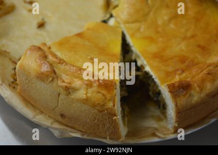 Una torta fatta in casa con un impasto sottile e un ripieno di verdure composto da cavolo, pezzi di funghi e cipolle in una cucina elegante. Foto Stock