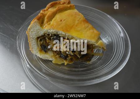 Un pezzo di torta fatta in casa con impasto sottile e ripieno vegetale composto da cavolo, pezzi di funghi e cipolle poste su un bicchiere trasparente Foto Stock