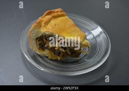 Un pezzo di torta fatta in casa con impasto sottile e ripieno vegetale composto da cavolo, pezzi di funghi e cipolle poste su un bicchiere trasparente Foto Stock