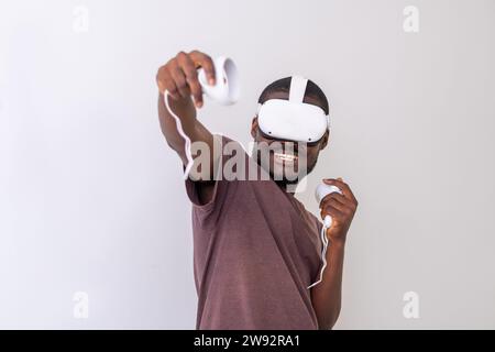 L'eccitante uomo nero che indossa un visore VR che gioca ai controller di gioco di realtà virtuale. Uomo che gioca a videogame online. Concetto di gaming VR Foto Stock