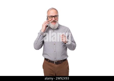 un uomo maturo dai capelli grigi con barba e baffi nei pantaloni e una camicia parla al telefono Foto Stock