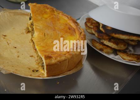 Una torta fatta in casa con un impasto sottile e un ripieno di verdure composto da cavolo, pezzi di funghi e cipolle in una cucina elegante. Foto Stock