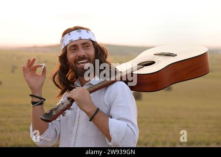 Elegante uomo hippie con fumante chitarra in campo Foto Stock