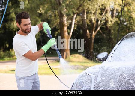 Uomo che copre l'automobile con schiuma all'autolavaggio esterno Foto Stock