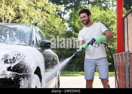 Uomo che copre l'automobile con schiuma all'autolavaggio esterno Foto Stock