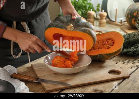 Donna che rimuove i semi dalla zucca cruda al tavolo di legno in cucina, primo piano Foto Stock