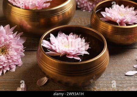 Ciotole tibetane con acqua e bellissimi fiori su un tavolo di legno, primo piano Foto Stock